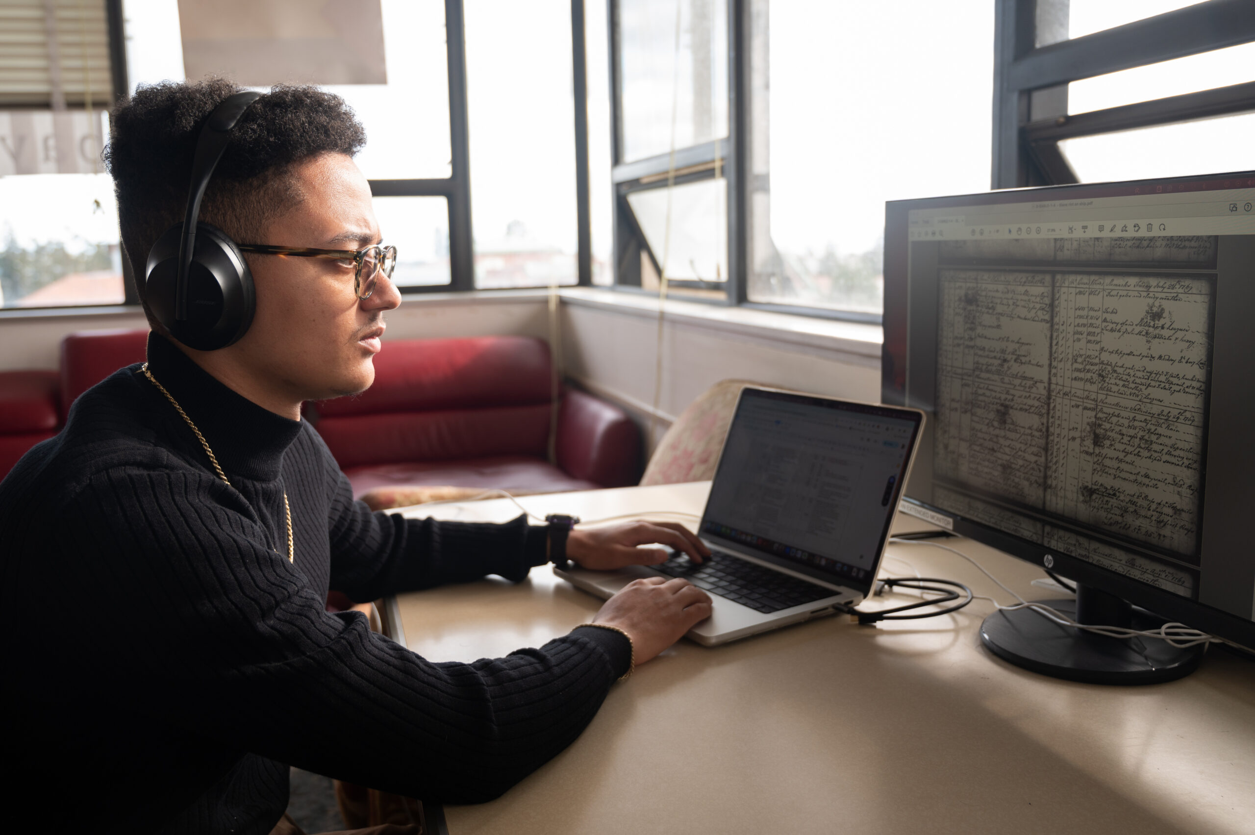 William Carter wears headphones and listens as a computer program reads text from transcribed slave ship logs, the original of which is displayed on a computer screen.