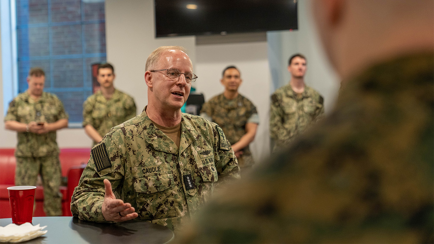 Admiral Daryl Caudle speaks directly to a Naval ROTC midshipman while others look on in the background