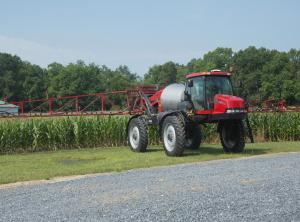 red agricultural sprayer in front of corn field with booms out