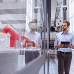 brand image - person walking down a hallway with a device, looking through window at manufacturing equipment