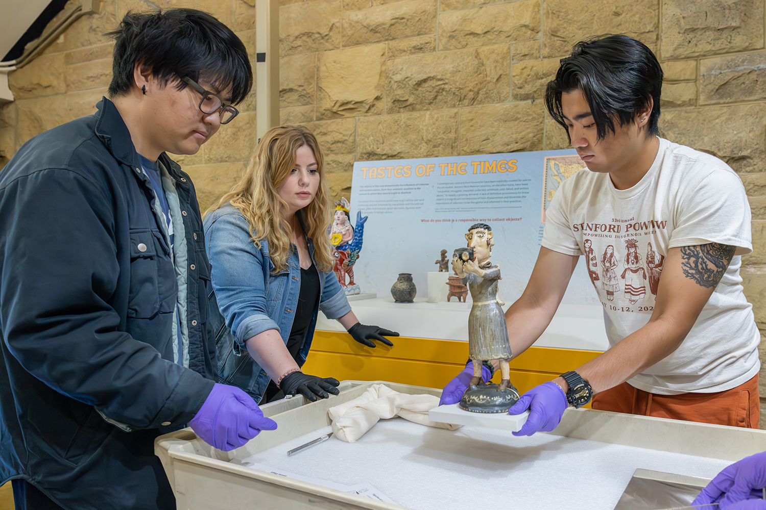 Image depicts students and staff lifting a figurine of a woman into a case.