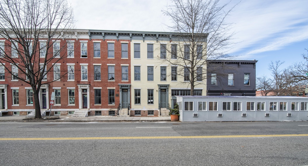 Streetscape of a row of three-story homes on a clear day, from across a 3-lane street