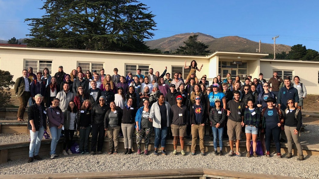 A large group of people pose for a photo outside a single-story building