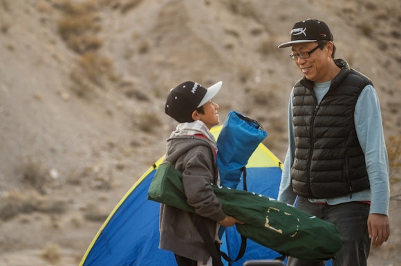 A father and son smile at each other in front of a tent