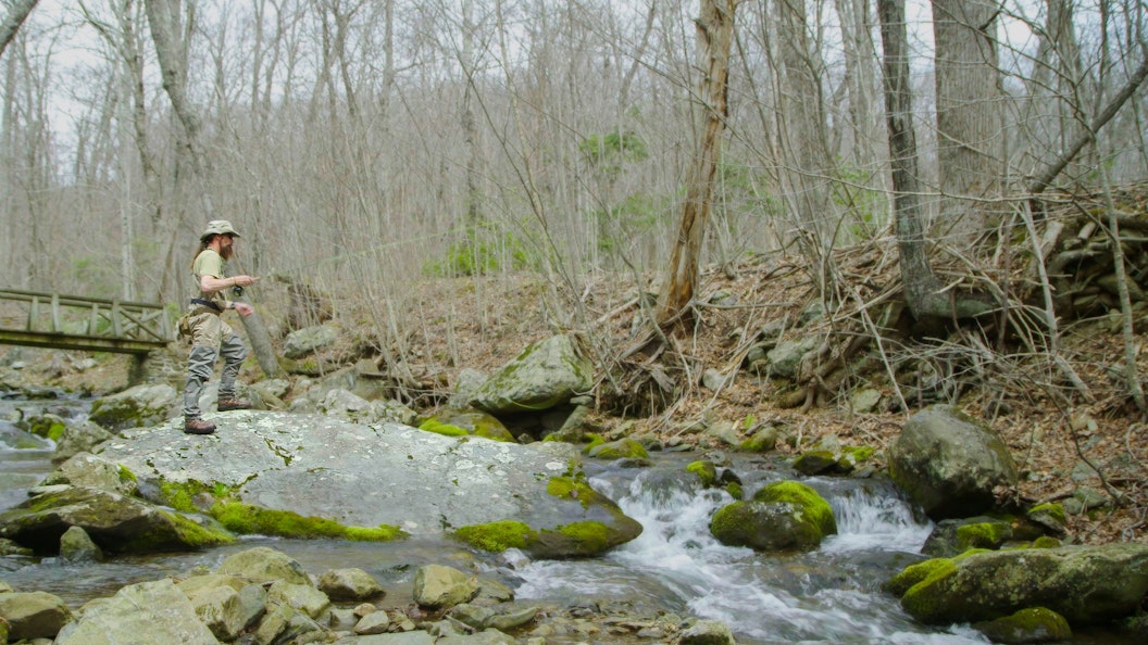 A person fly fishes along a rocky stream