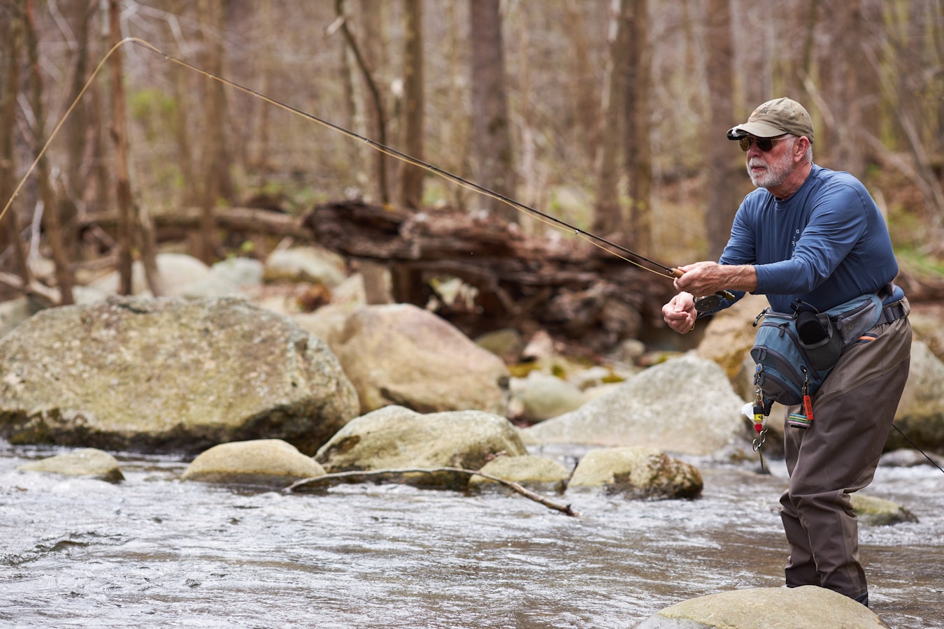 A person goes fly fishing in a stream that reaches up to his knees