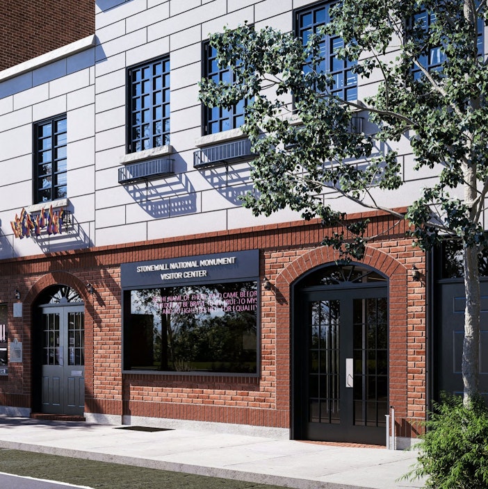 A red and white brick building with a window sign that reads "Stonewall National Monument Visitor Center." In the front window, the neon sign in the center reads: “In the name of those who came before me, I pledge to be brave, to be true to myself, and to fight like hell for equality.”