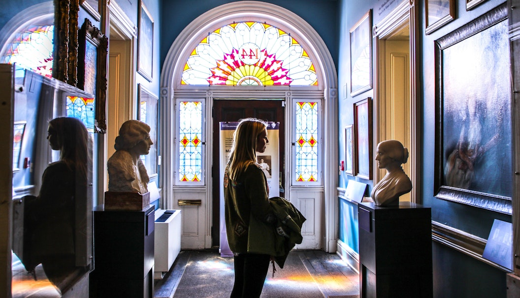 Visitor in a hallway with numerous paintings and busts of suffragists