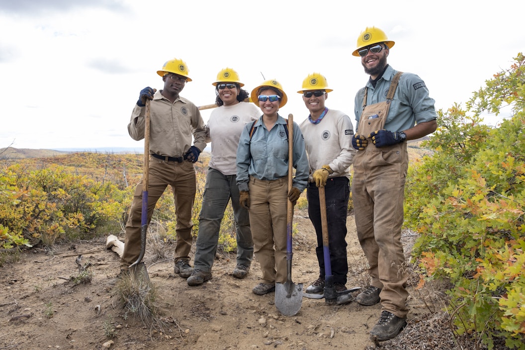 A group of people, wearing hard hats and some holding shovels, pose for a photo