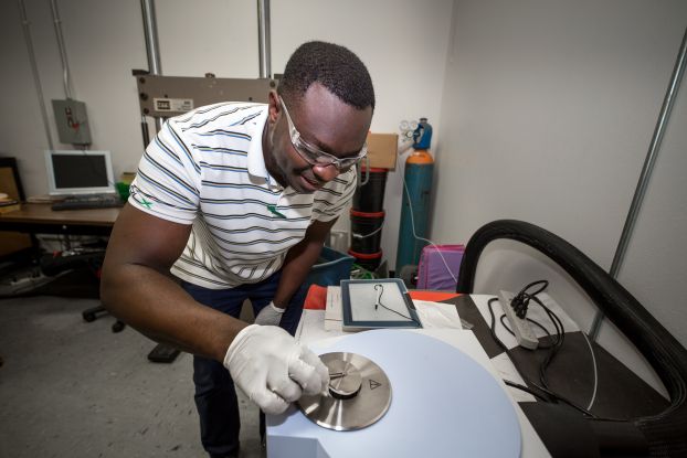 A man stands above a piece of laboratory equipment, lifting the lid off with tweezers