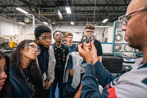 Closeup of tour guide demonstrating gas flow control system to students in safety glasses