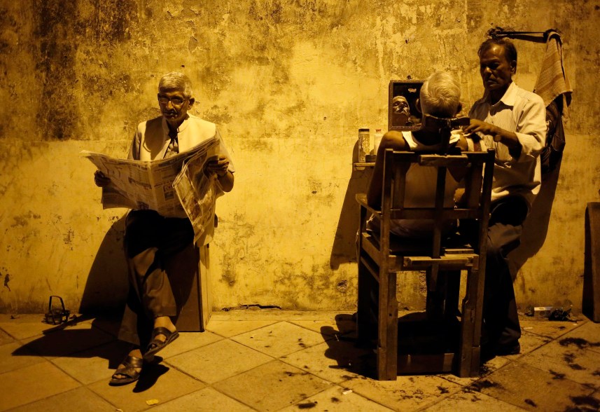 A man gets his shave done by a roadside barber as another reads a newspaper while waiting for his turn, in New Delhi August 20, 2014. REUTERS/Anindito Mukherjee (INDIA - Tags: SOCIETY TPX IMAGES OF THE DAY)