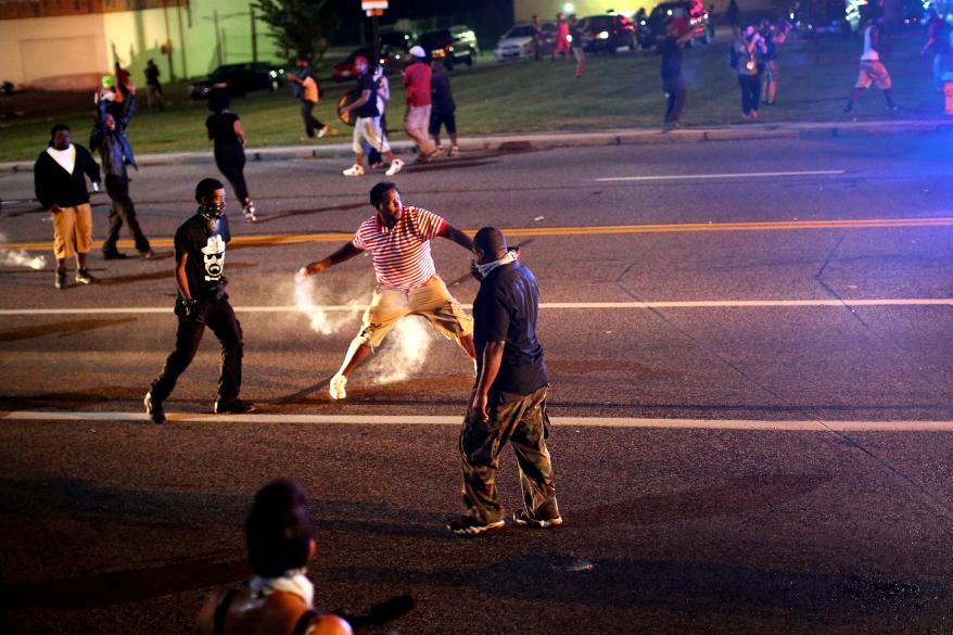 Protesters try to throw tear gas grenades back towards the police.