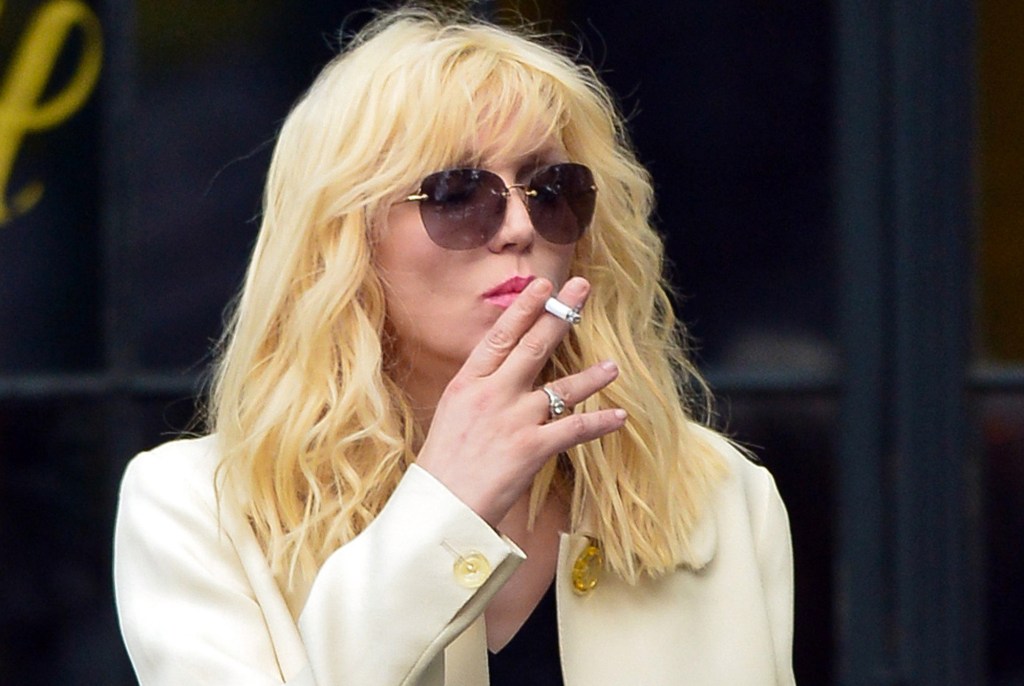 Courtney Love smokes a cigarette in a white jacket.