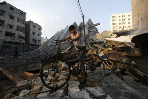 A young Palestinian man walks with his bicycle over the remains of Al-Basha, a building that was destroyed by an Israeli air strike in Gaza City on August 26.