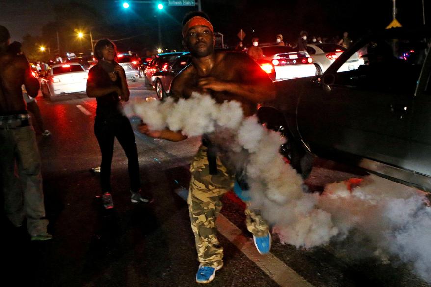 A protester tries to throw tear gas back at the police.