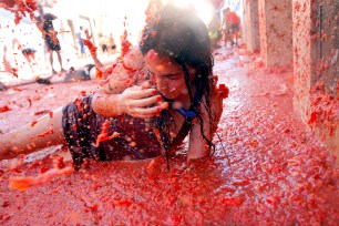 A woman lays in a puddle of tomato juice during the annual "tomatina" tomato fight fiesta in the village of Bunol, 50 kilometers outside Valencia, Spain, Wednesday, Aug. 27, 2014. The streets of an eastern Spanish town are awash with red pulp as thousands of people pelt each other with tomatoes in the annual "Tomatina" battle that has become a major tourist attraction. At the annual fiesta in Bunol on Wednesday, trucks dumped 125 tons of ripe tomatoes for some 22,000 participants, many from abroad to throw during the hour-long morning festivities. (AP Photo/Alberto Saiz)