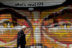 An elderly woman walks past a graffitied wall with a freshly painted "What's next???" message in central Athens on July 13.