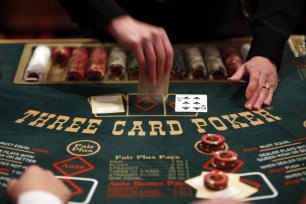 A dealer flips cards at a three card poker table