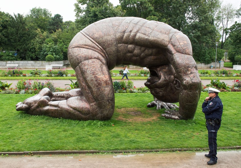 A policeman stands in front of the sculpture "Bending Man" in Duesseldorf, Germany.