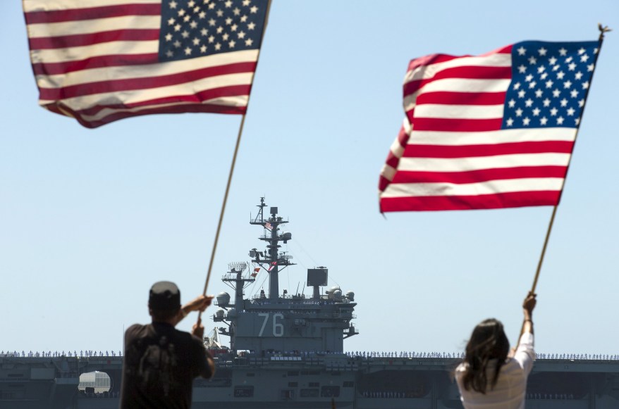 Supporters wave American flags at the USS Ronald Reagan, a Nimitz-class nuclear-powered super carrier, as it departs from San Diego.