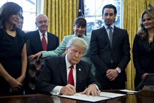 Donald Trump signs an executive order while surrounded by small business leaders in the Oval Office.