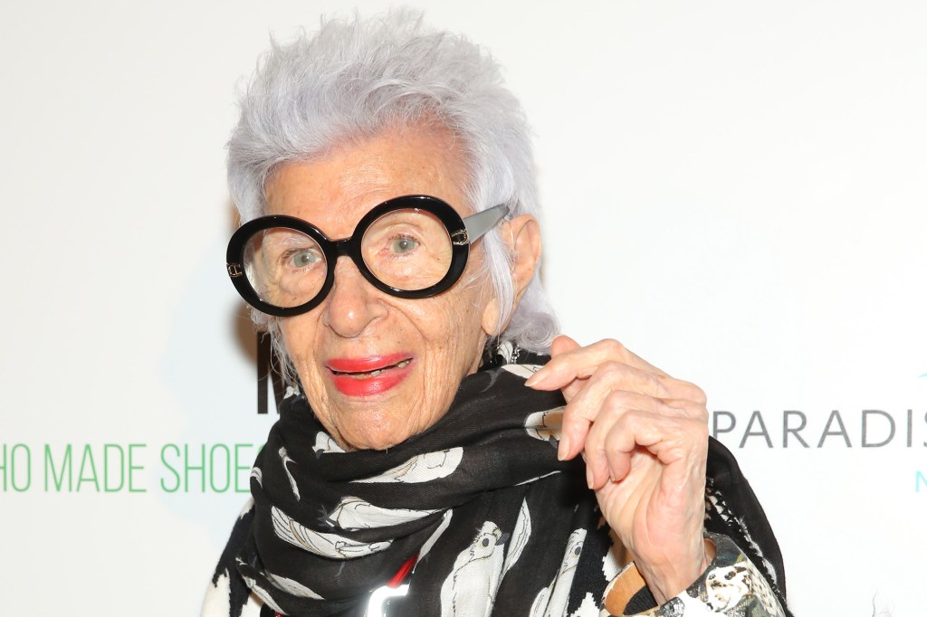 Iris Apfel wearing glasses and a black outfit standing in front of a red carpet at the Manolo: The Boy Who Made Shoes for Lizards premiere in New York.