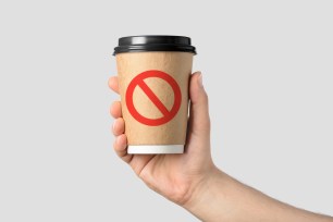 Image of someone holding a plastic coffee cup with a red ex through it.