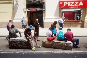 Presumably homeless individuals rest on stone blocks at the newly reinstalled pedestrian plaza on West 32nd Street near Penn Station.