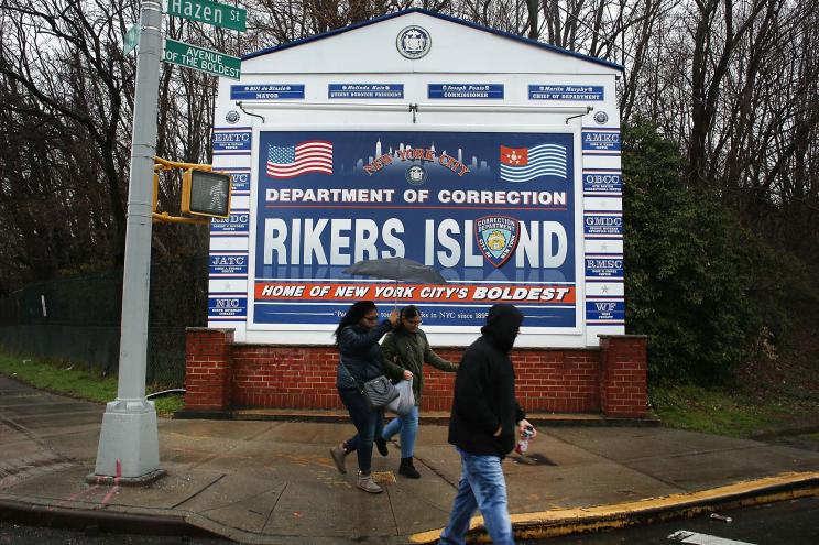 People walk by a sign at the entrance to Rikers Island.