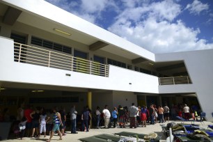 People whose homes are unsafe to enter after the previous day's magnitude 6.4 earthquake line up for lunch in an outdoor area of the Bernardino Cordero Bernard High School, which is being used as a shelter despite no electricity in Ponce, Puerto Rico.