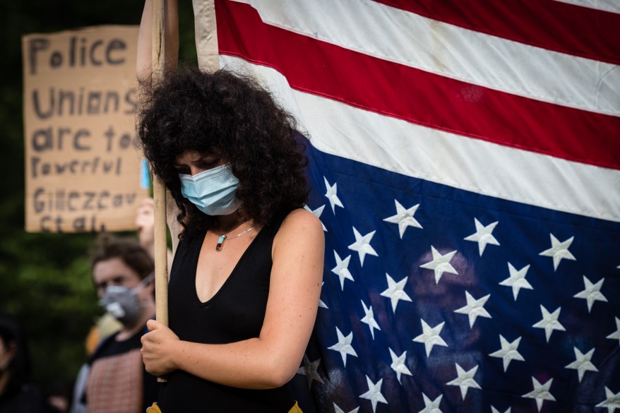 A protester holding an upside down American flag bows her heard during a moment of silence in the West Village, Manhattan on Thursday June 11, 2020 in New York City.