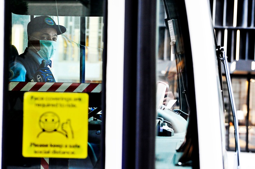 A MTA city bus driver wears a protective mask as the posted sticker on the door requests of all riders.