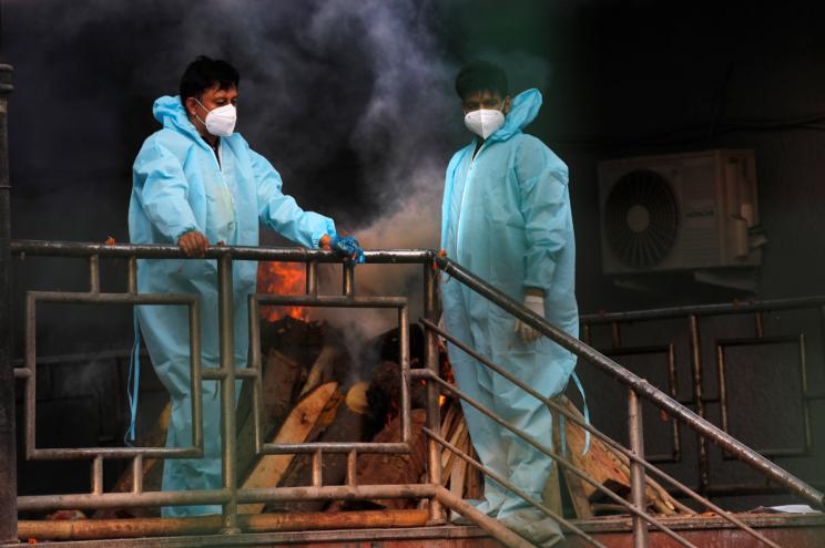 People wait by the burning pyre of a relative who died of coronavirus, at a crematorium in New Delhi, India.