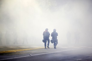 Two police officers in riot gear walk through a cloud of tear gas during a demonstration over recent grand jury decisions in police-involved deaths on December 7, 2014 in Berkeley, California.