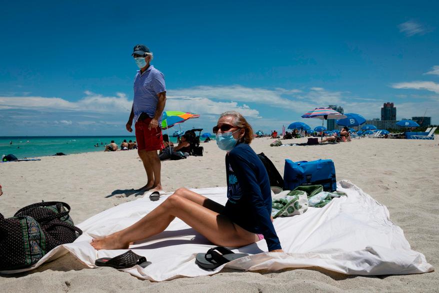 Diane, a nurse from Houston, Texas, sunbathes at the beach next to her husband, both wearing face masks, in Miami Beach, Florida.