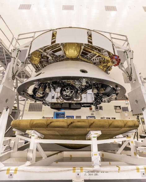 The Mars 2020 Perseverance rover mission's disk-shaped cruise stage sits atop the bell-shaped back shell, which contains the powered descent stage and Perseverance rover. Below is the brass-colored heat shield that is about to be attached to the back shell.