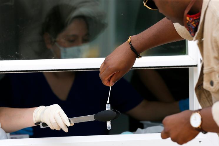 Parkland Hospital employees, sitting behind window, collect a self administered test sample from a man at a COVID-19 walk up testing site in Dallas, Thursday, June 11, 2020.