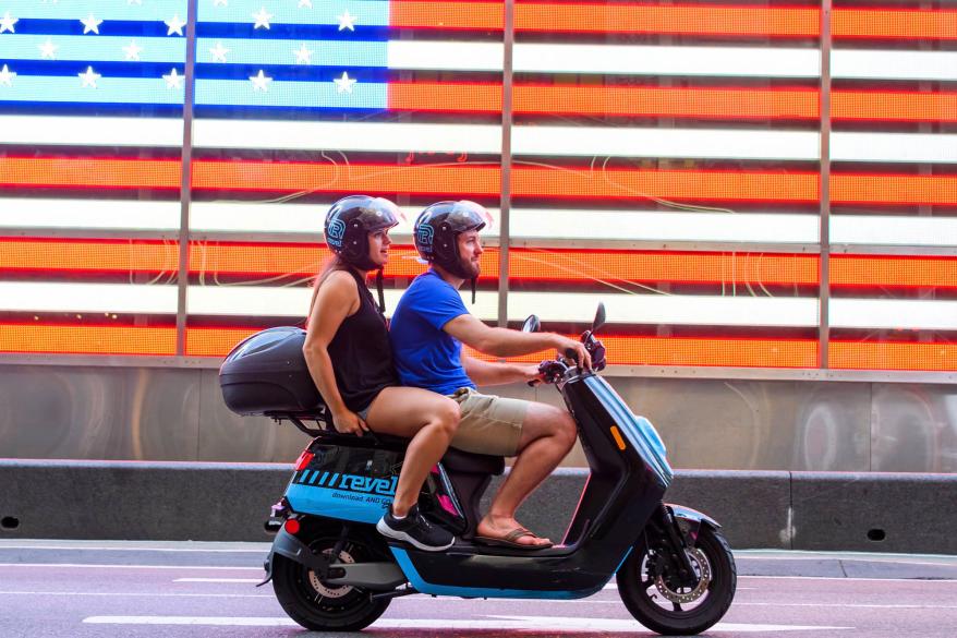 People ride a Revel scooter in Times Square