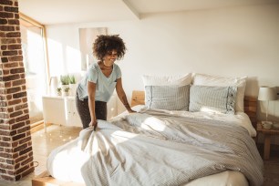 Young woman making bed at home.