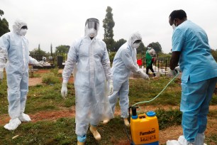 Health workers sanitize their Personal Protective Equipment (PPE), after the cremation of a body in Nairobi, Kenya.