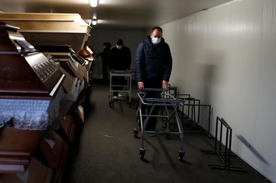 Workers walk past caskets placed inside an overflow cold storage container placed outside a crematorium in Ostrava, Czech Republic, Thursday, Jan. 7, 2021.