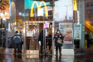 People wearing masks stand outside a McDonalds in Times Square during a snow storm