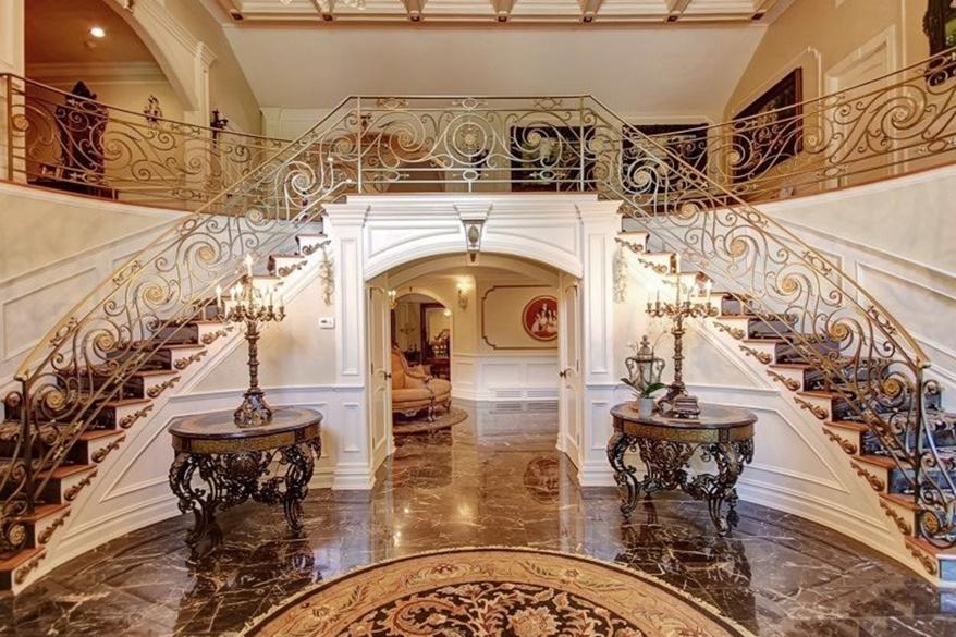 The inside of the front door has sculpted wings as handles, which open onto a black marble floor and a two-story foyer with a Cinderella staircase.