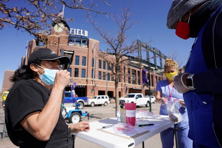 A woman self-administers a swab for a COVID-19 test at a table set up outside the main gate of Coors Field as fans return for the first time to the ballpark for a baseball game between the Los Angeles Dodgers and the Colorado Rockies Thursday, April 1, 2021, in Denver.