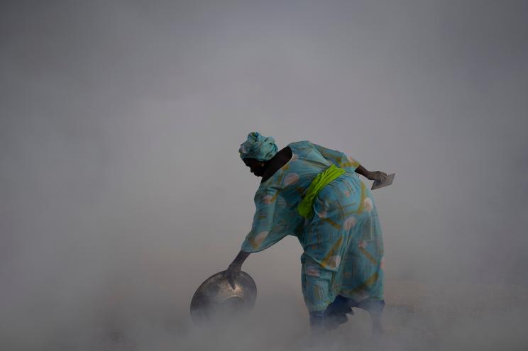 Ndeye Yacine Dieng drops embers over peanut shells covering fish as she walks amidst the smoke on Bargny beach, some 35 kilometers (22 miles) east of Dakar, Senegal, Wednesday April 21, 2021.