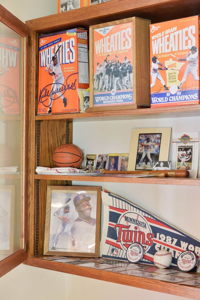 The living room has a collection of memorabilia including baseballs, mini-bats, Twins champion pins, Puckett portraits, baseball cards, Puckett Wheaties cereal boxes and other memorabilia.