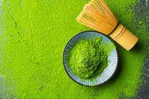 green matcha powder in a bowl and on the background and a traditional whisk