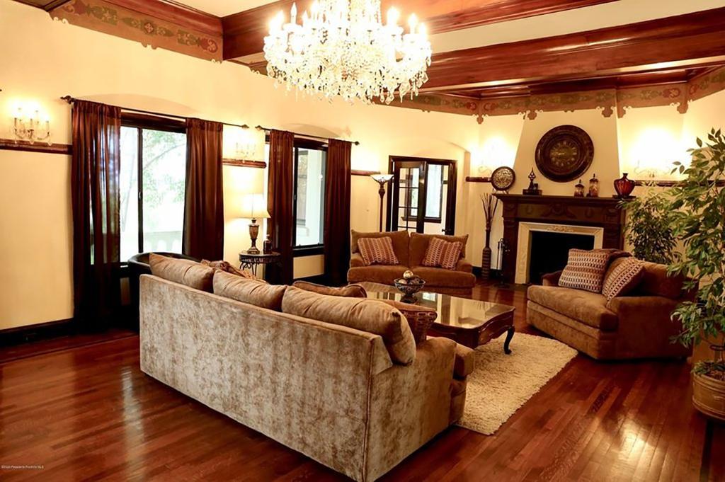 The living room has exposed ceiling beams, a grand chandelier, a carved wood mantle fireplace and large french doors.