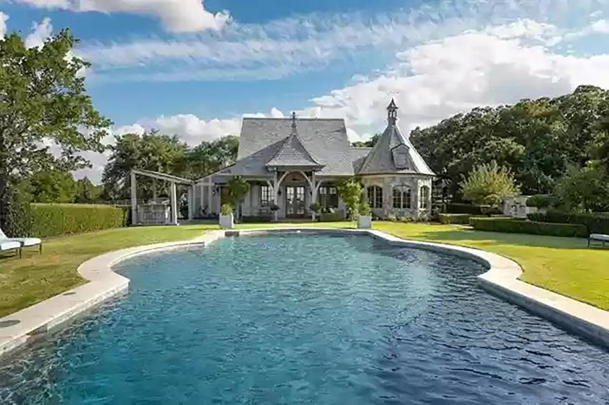 The house opens through a covered patio to an irregularly-shaped pool with a cabana.